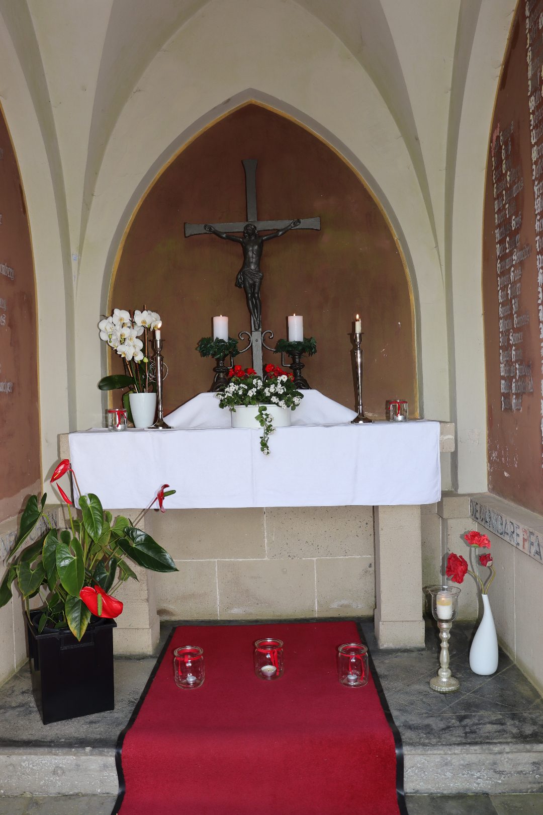 Festlich geschmückter Altar der Pestkapelle mit Kruzifix, weißen Orchideen und roten Blumen
