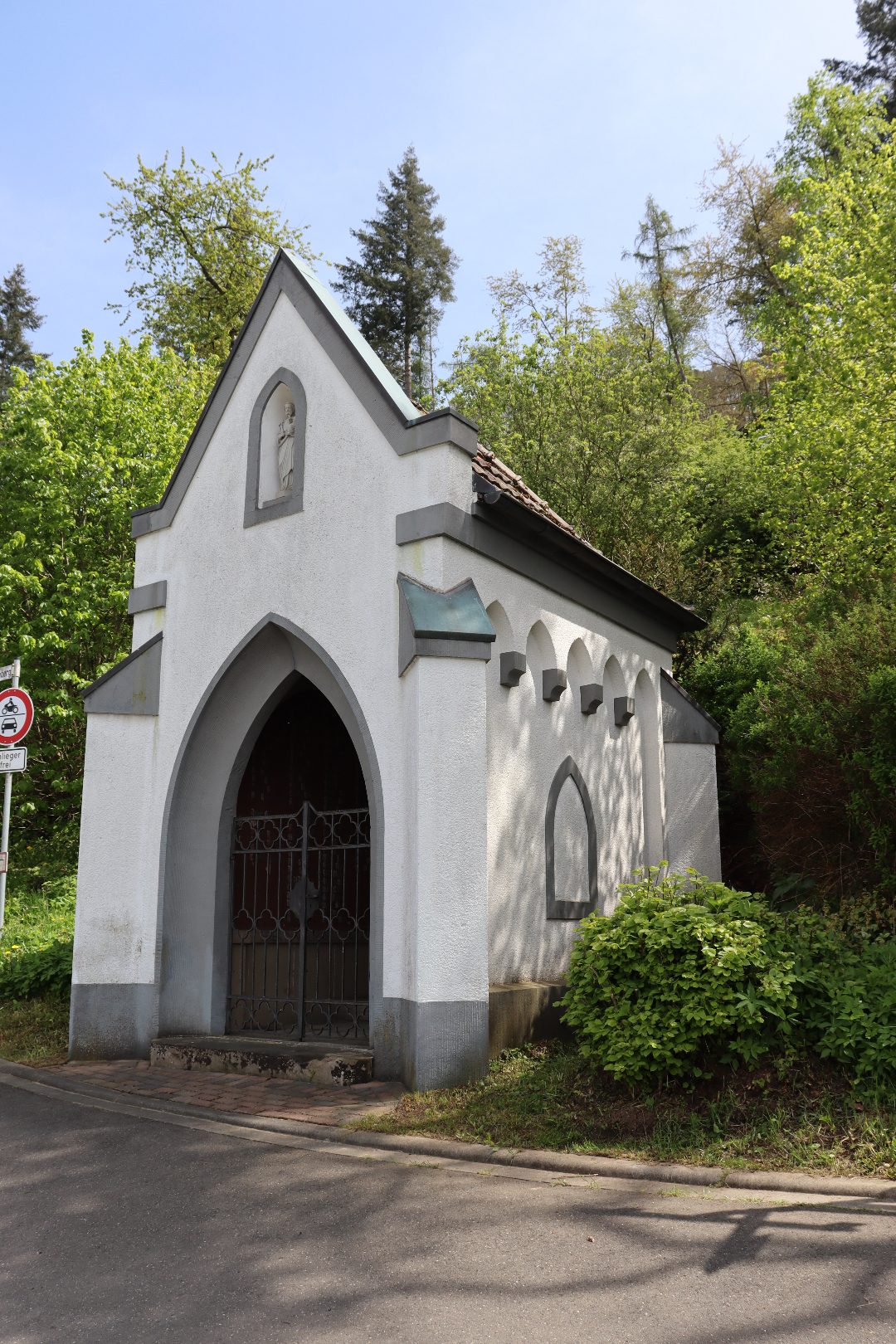 Frühjahrsfoto der Pestkapelle: weißer Bau mit neogotischem Portal und Heiligennische, umgeben von frischem Grün
