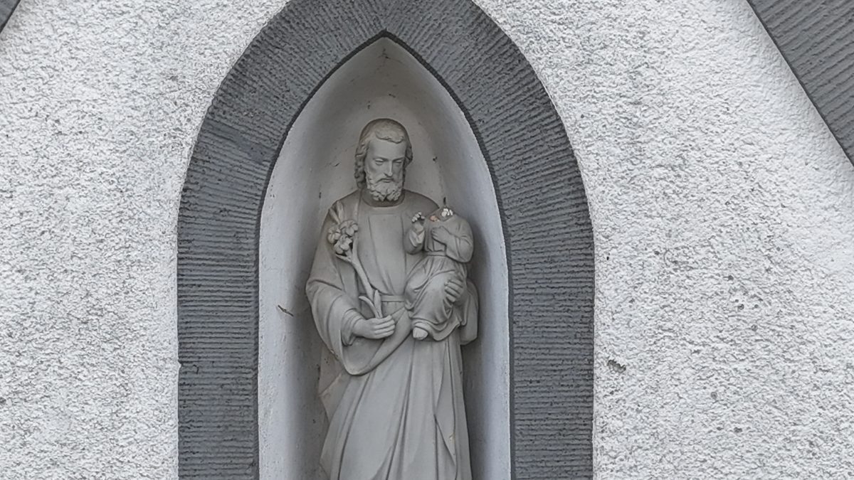 Nahaufnahme der Giebelfigur: Hl. Josef hält das Jesuskind und einen Lilienzweig